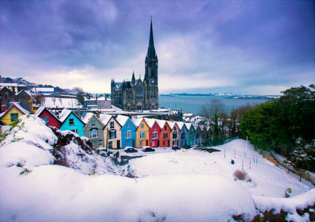 a winter scene showing a line of houses, each a different colour, and a church in the background